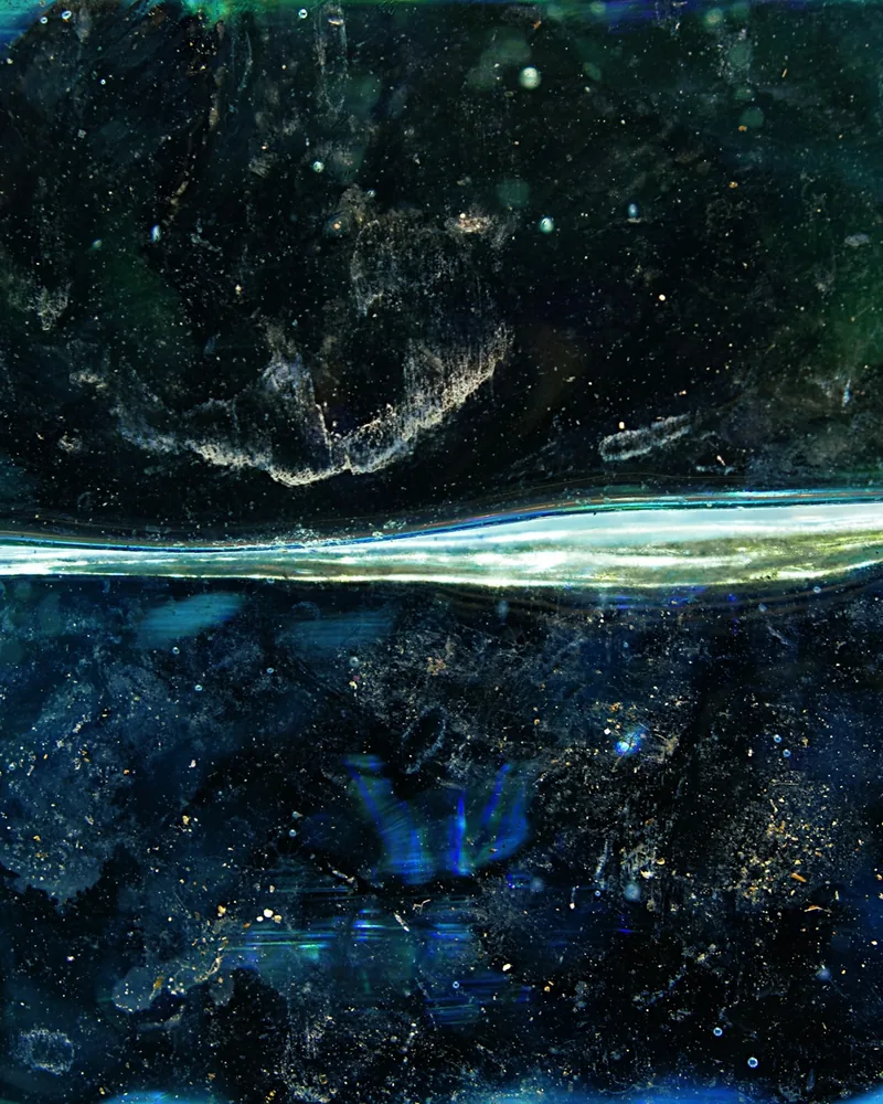 Detalle macro de dos capas de vidrio fundido en tonos azules y verdes con pequeñas burbujas atrapadas y una línea de unión brillante